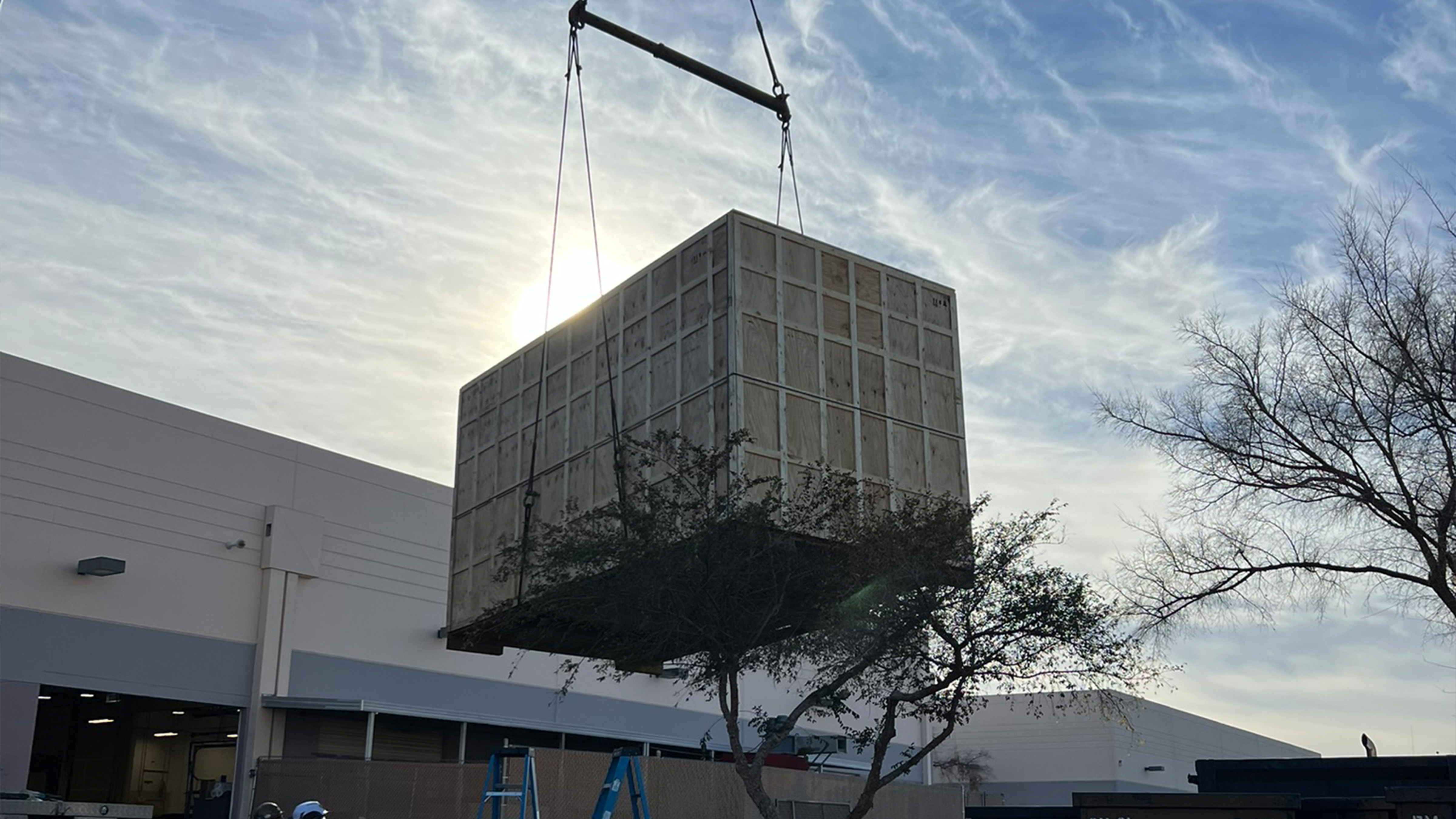 Oversized wood crate lifting construction equipment by crane, designed for rugged transport and protection in industrial environments.