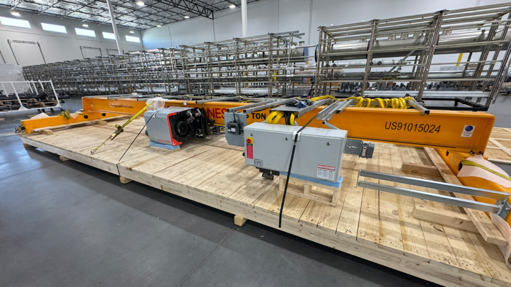 Yellow 10-ton overhead crane components strapped to a custom wood skid for industrial transport inside a warehouse
