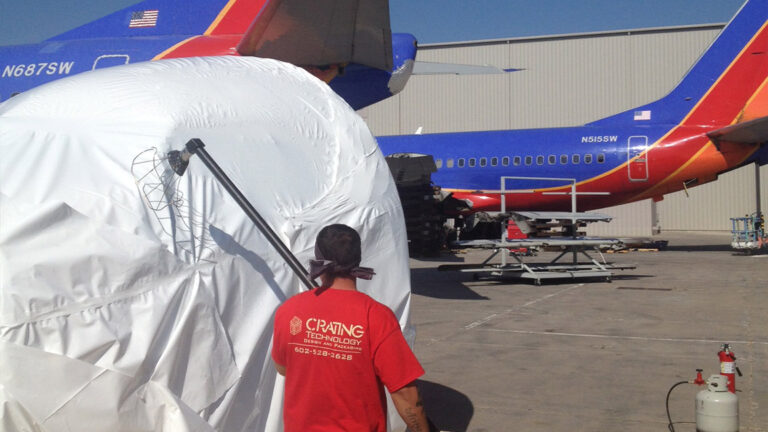 A Crating Technology specialist shrink-wrapping a Southwest Airlines cockpit directly on the airport tarmac for secure transport.