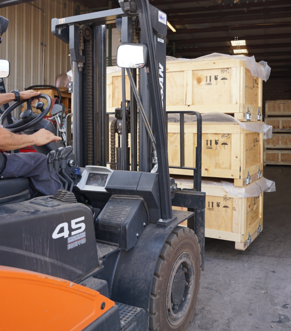 Forklift operator moving large wooden crates inside a warehouse.